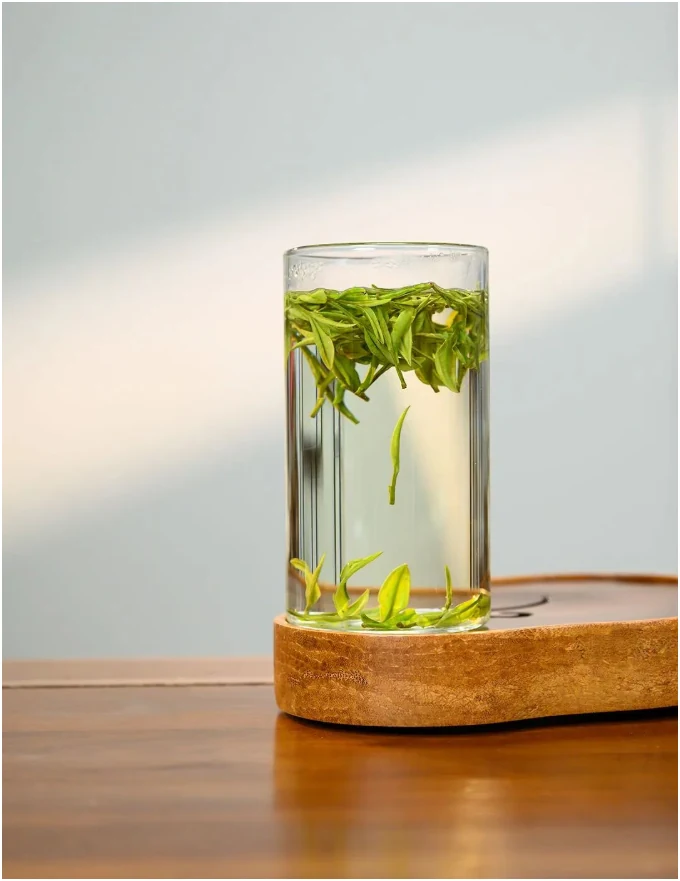 A clear glass of green tea on a wooden coaster in soft light