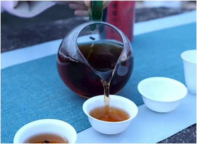 Amber Liubao tea being poured from a glass pitcher into white cups