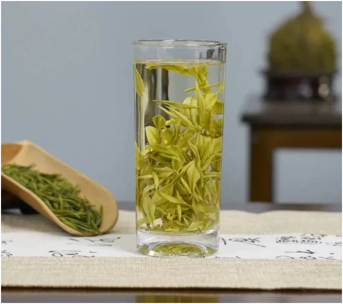 Anji Bai Cha brewing in a tall glass beside a wooden scoop