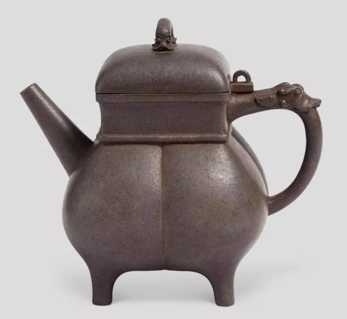 Dark clay teapot on four feet with a square upper body and sculpted dragon-head handle