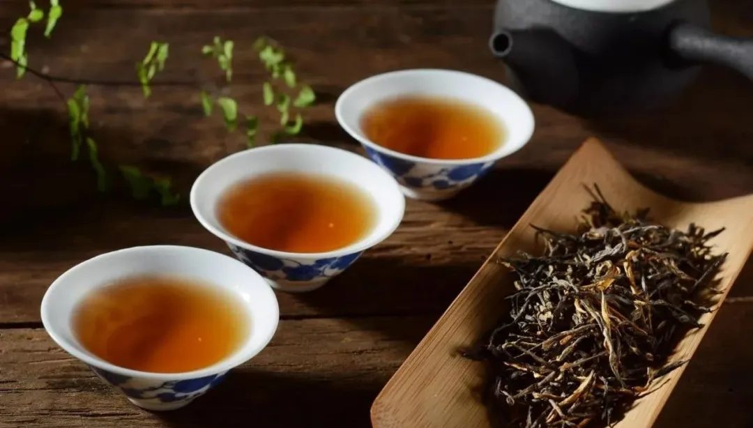 Three blue-and-white cups of amber tea beside dry leaves and a dark teapot
