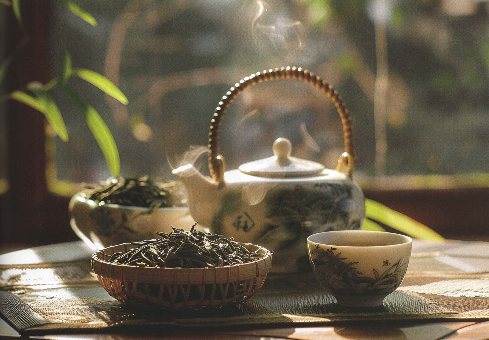 Steaming ceramic teapot, cup and baskets of loose-leaf tea