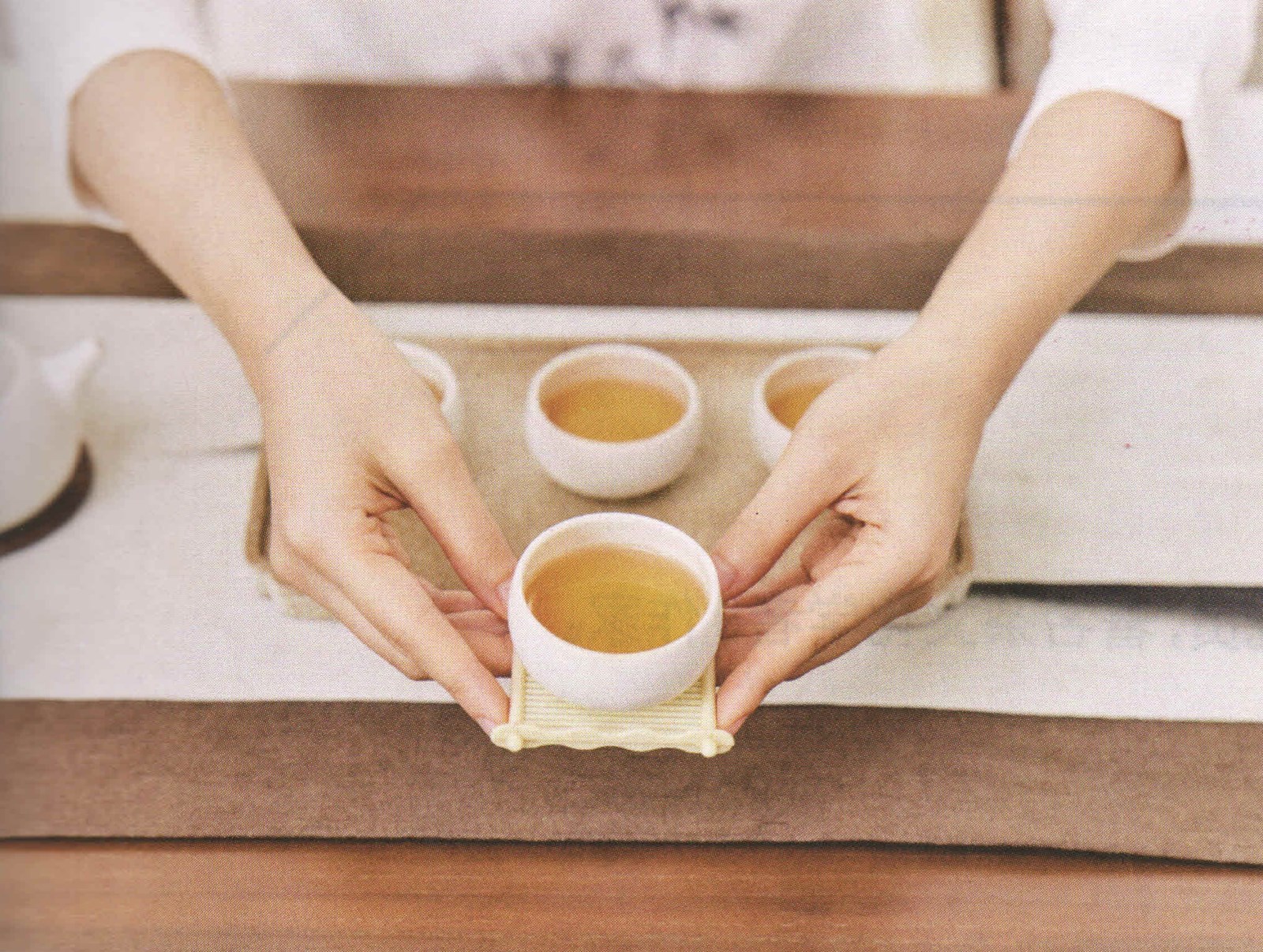 Hands offering a cup of tea on a woven coaster