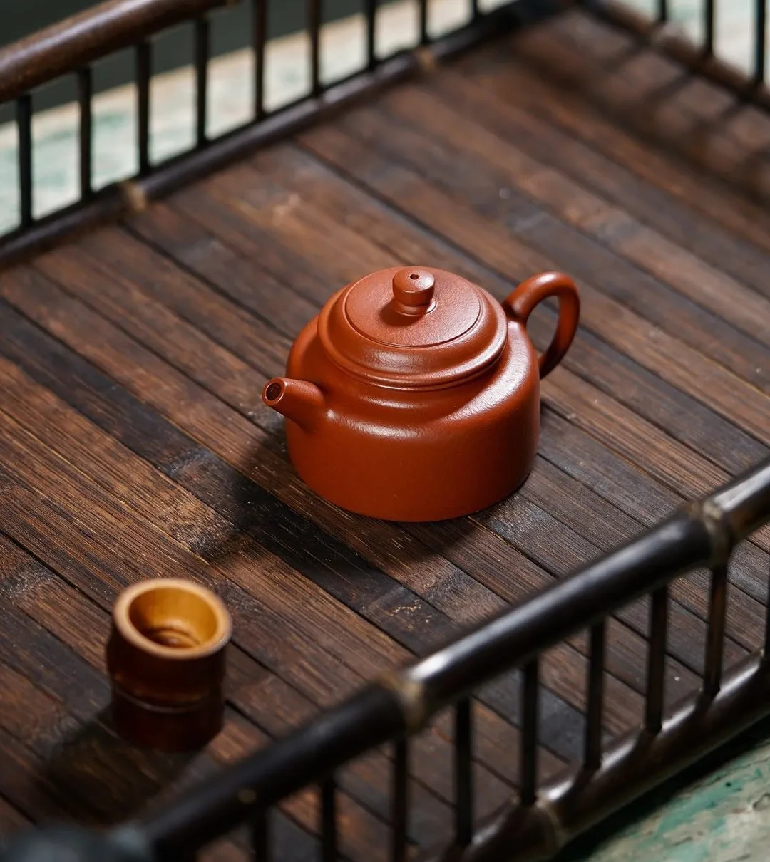 Cylindrical red clay teapot with a straight spout on a wooden tray