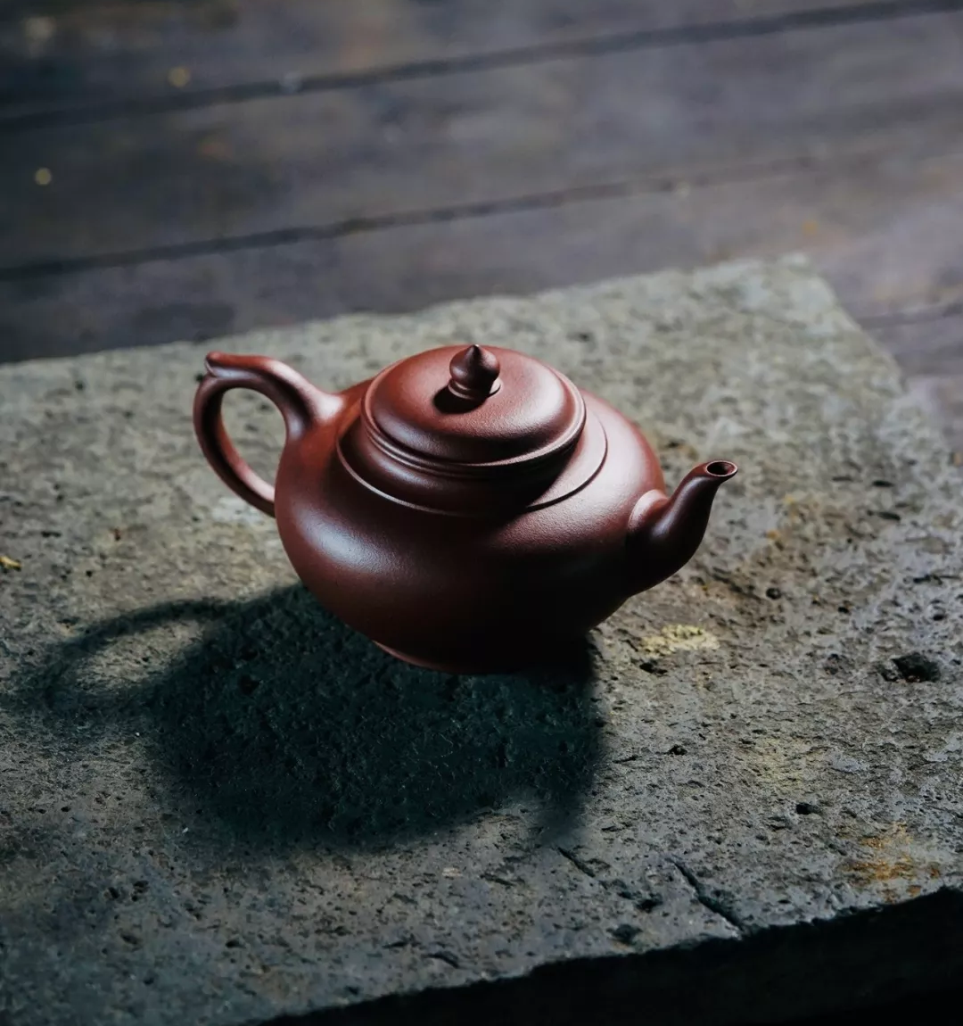 A rounded dark reddish-brown teapot on a stone slab
