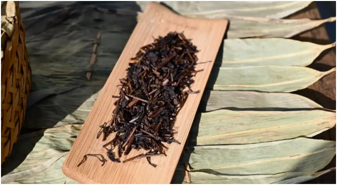 Dark Ancha leaves in a wooden scoop above ruoye leaf wrappers