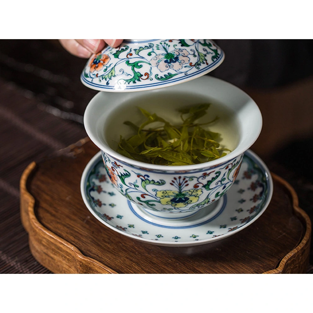 Le couvercle relevé pour révéler un intérieur doucai fleuri gaiwan rempli de thé