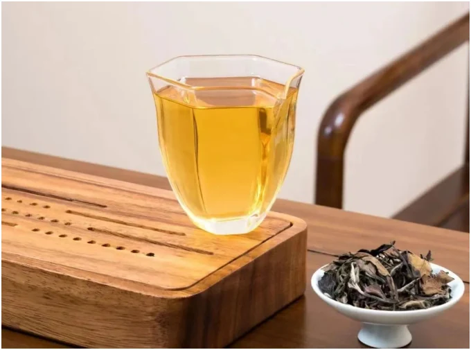 Golden white tea in a faceted glass beside dry leaf