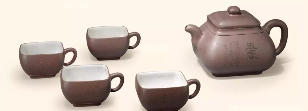 Rounded-square clay teapot with engraved calligraphy and four matching pale-interior cups
