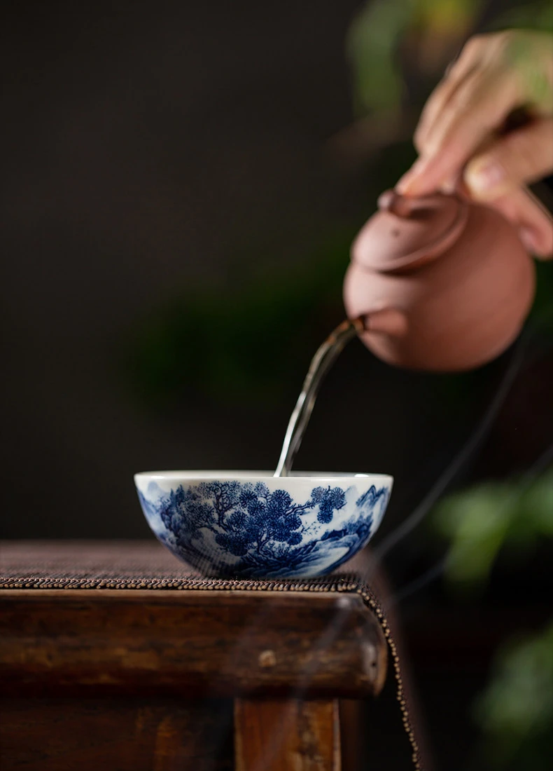Tea being poured from a clay teapot into the landscape teacup