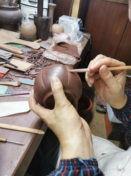 Hände verfeinern die Außenkontur eines ungebrühten Formkörpers Yixing ton teekanne mit einem kleinen Werkzeug