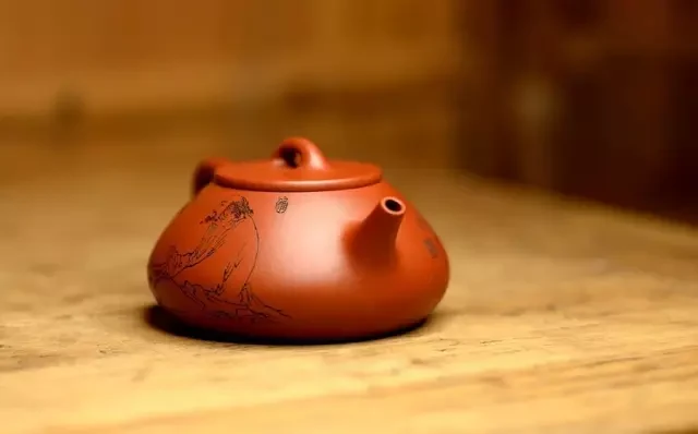 Couleur orange rougeâtre-rougeâtre, légèrement aplatie, théière avec une décoration gravée sur une table en bois