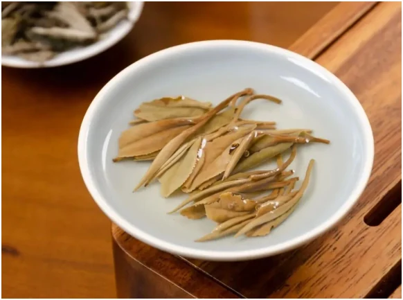 Infused white tea buds in a porcelain gaiwan on a wooden tray