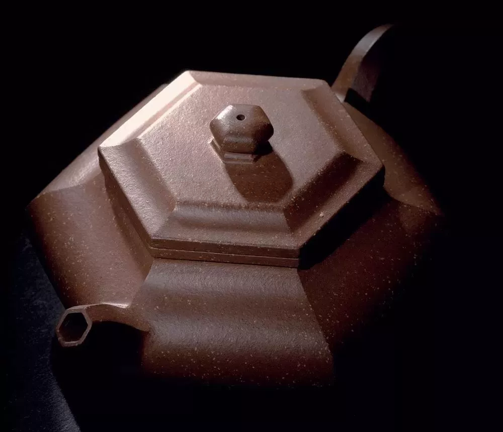 Oblique view of a six-sided clay teapot showing its layered lid, faceted knob and spout opening