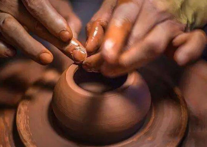 पोटर एक पहिए पर मिट्टी शरीर के किनारों को आकार दे रहा है