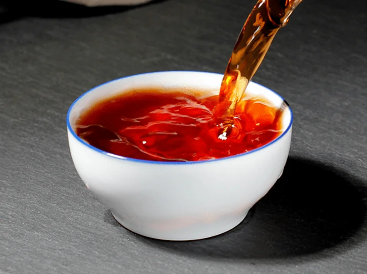 Dark amber tea being poured into a white cup