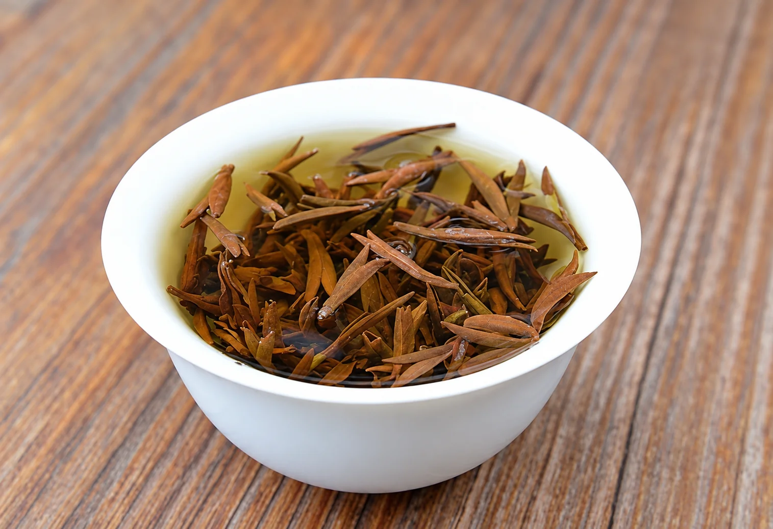 Opened tea buds and amber infusion in a white bowl