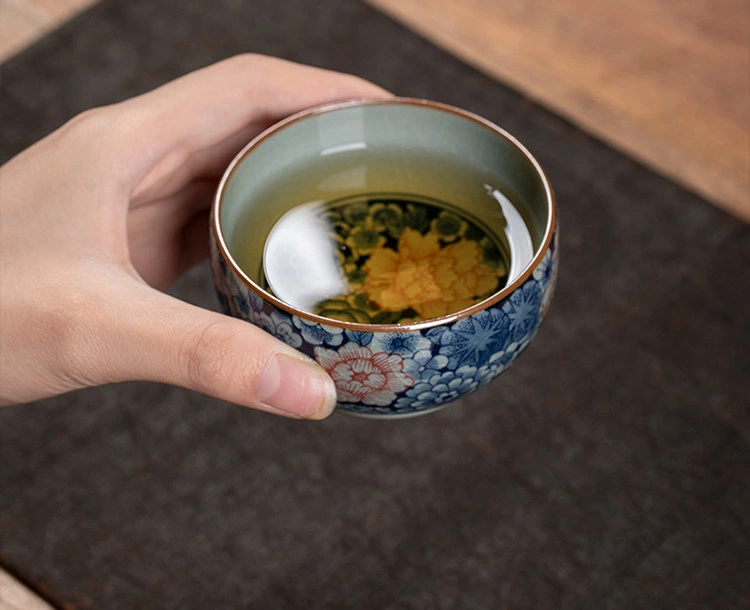 Hand holding the millefleurs teacup with tea over the painted interior flower