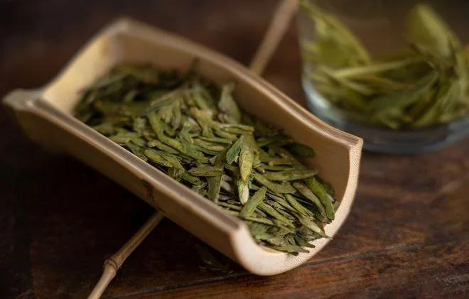 Dry green tea in a scoop beside glass teaware