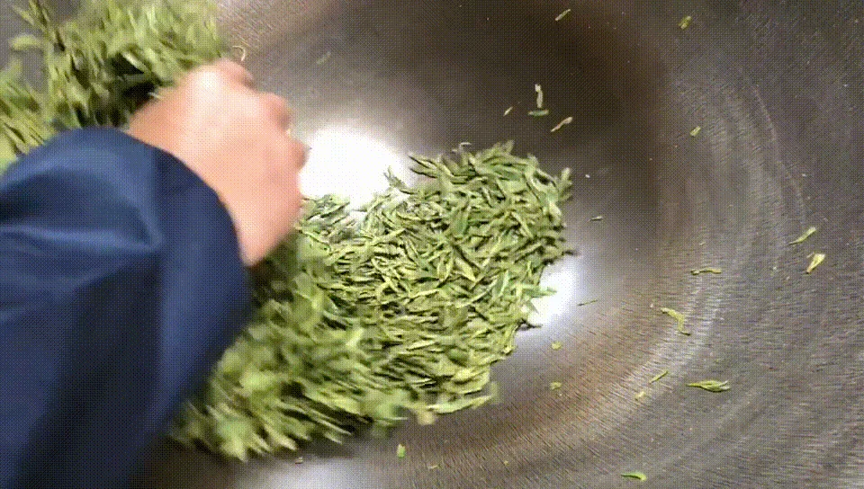 A hand working tea leaves in a heated pan
