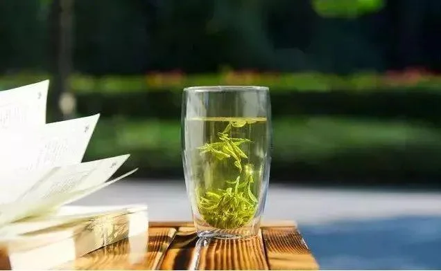 A glass of tea beside a book on a bamboo mat