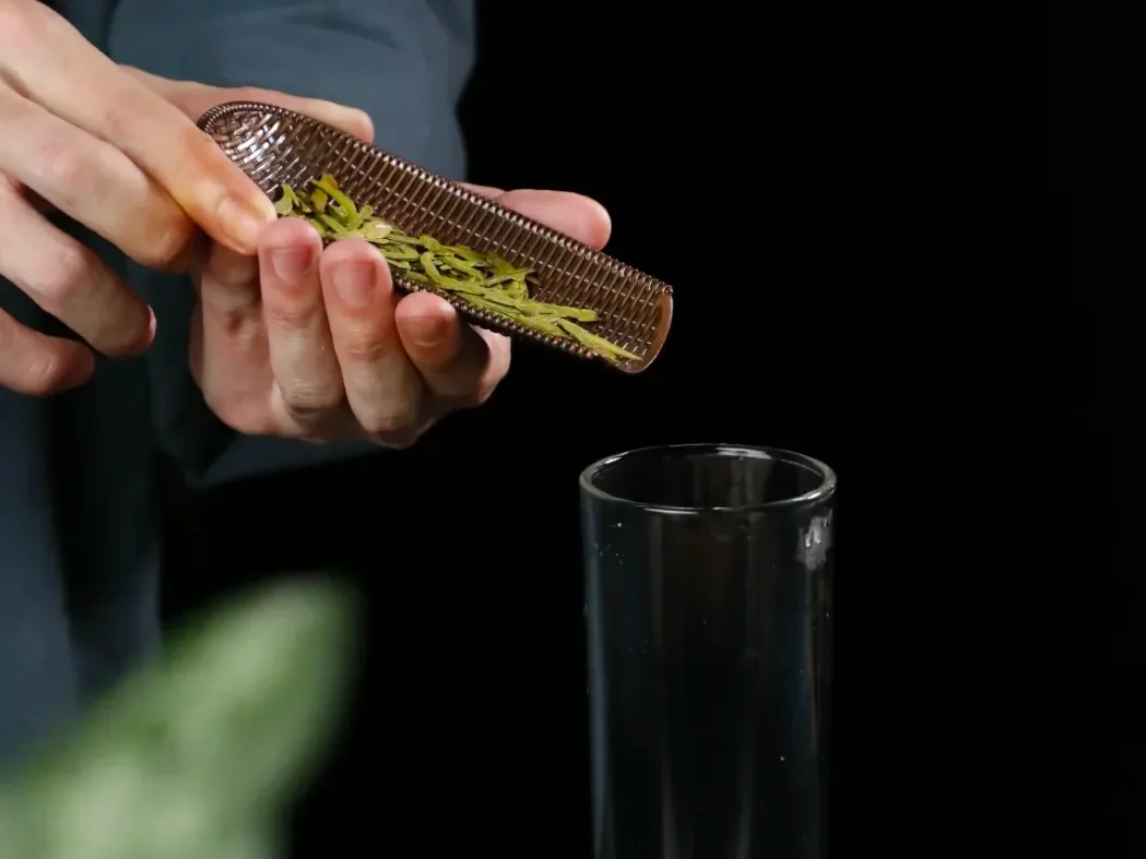 Tea leaves transferred from a scoop into glass teaware