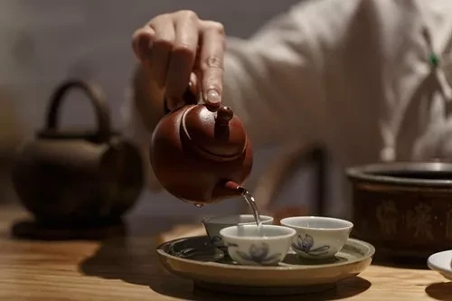 丸いトレイの上に小さな磁器製のカップ 陶土 茶壺 からお茶を注ぐ手が
