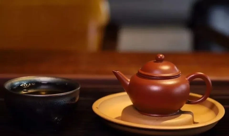 黄色の皿の上に丸みを帯びた赤褐色の茶葉 茶壺 が、暗い茶碗の横に置かれている。