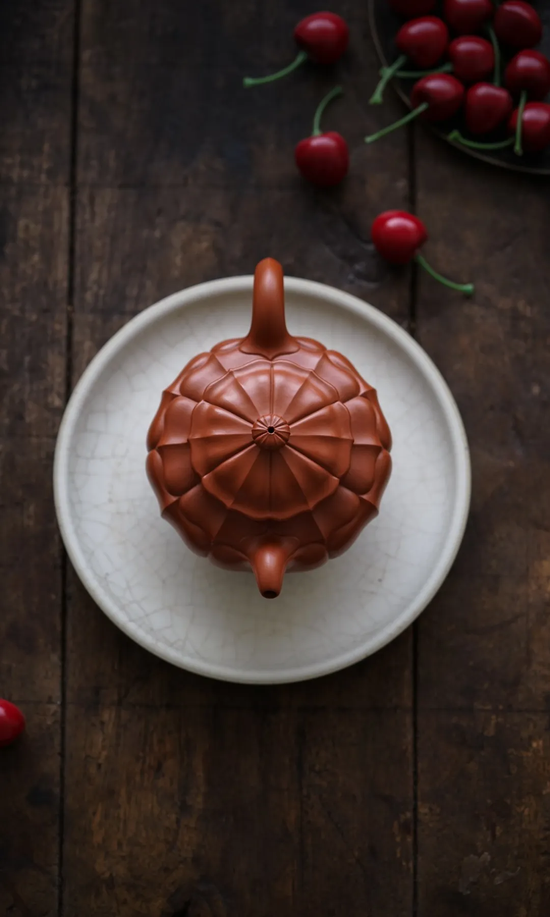 Top view of a ribbed reddish-brown teapot on a pale plate with cherries nearby