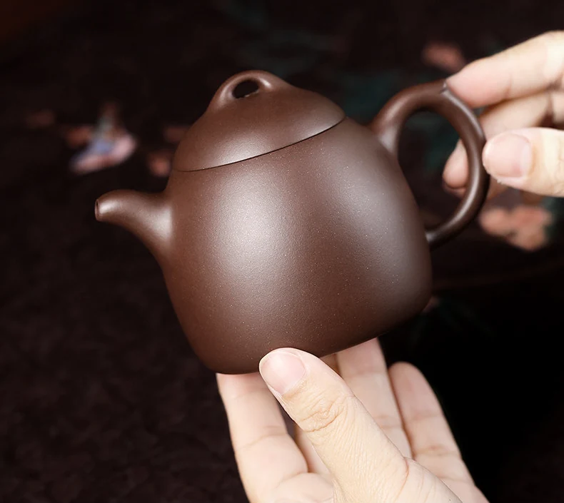 Qinquan purple clay teapot held in two hands to show its compact size