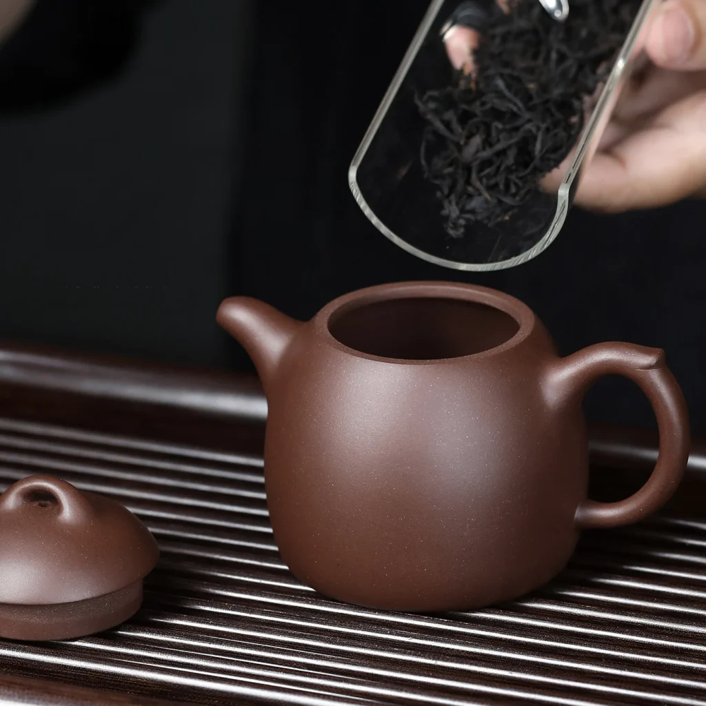 Open Qinquan Yixing teapot with its lid beside it as tea leaves are added