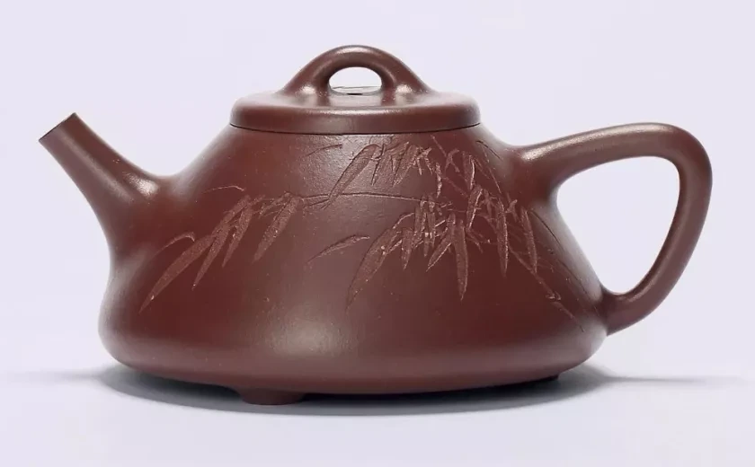 De perfil triangular, marrón tetera con bambú incisado, un pomo arqueado y un mango angular