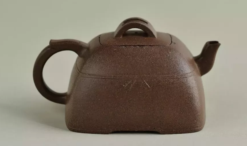 Low rounded-square brown teapot with an arched knob and incised decoration