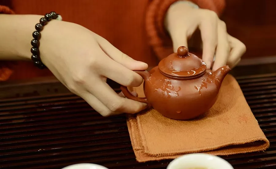 手のひらは赤い茶色で、柔らかいオレンジ色の茶巾の上に 宜興 茶壺 載っている。