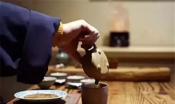 A hand pouring tea from a clay teapot into a tall cup