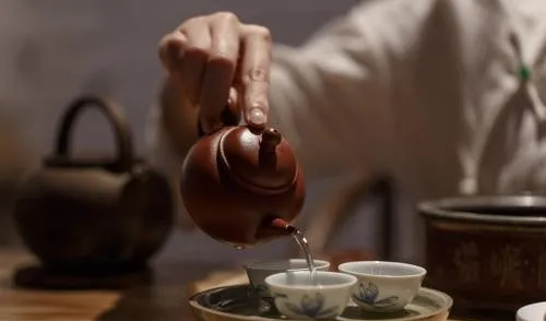 A small reddish-brown teapot pouring into porcelain cups on a tea tray