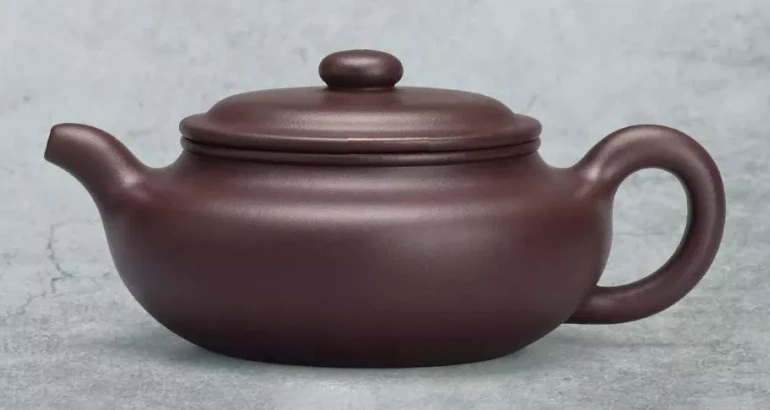 De color marrón claro, tetera con un cuerpo redondeado bajo, una boquilla curvada corta y asa anular