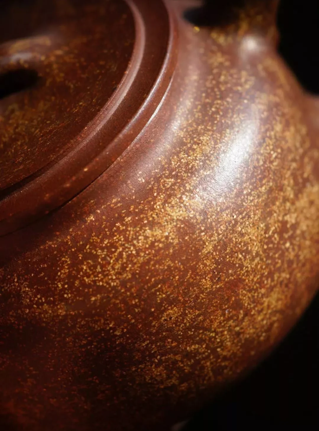 Close-up of a reddish teapot lid and shoulder covered with contrasting pale granules