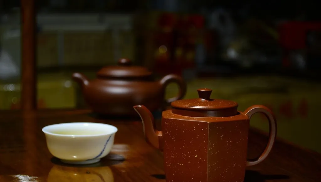 An angular reddish-brown teapot beside a porcelain cup on a wooden table