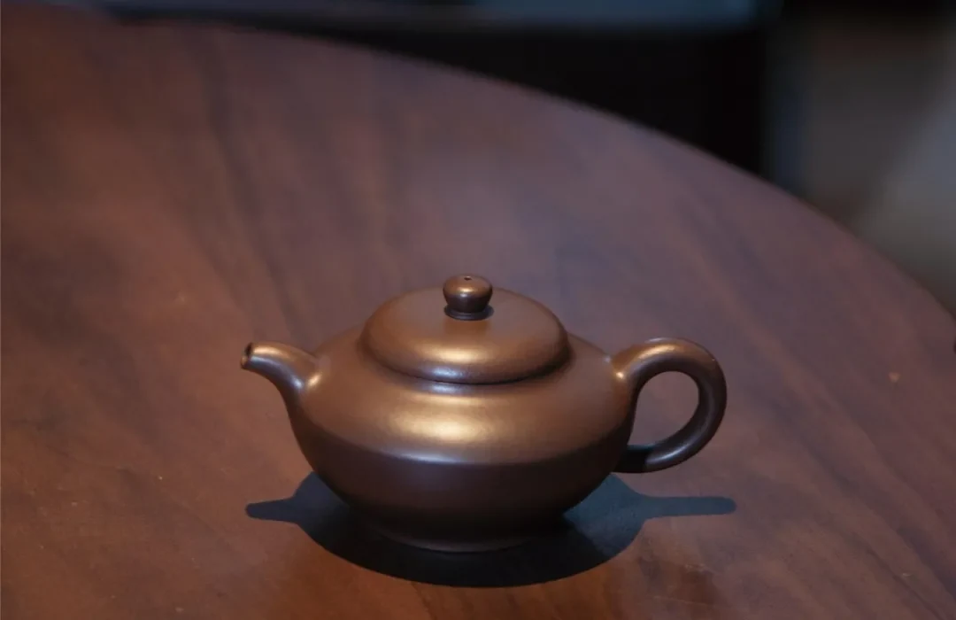 木製のテーブルの上に丸みを帯びた低めの茶色 陶土 茶壺 で、ドーム状の蓋が付いています。