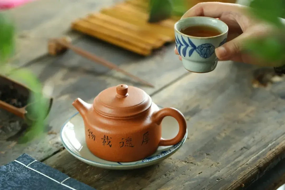 Yixing मिट्टी चायदानी लकड़ी के चाय की मेज पर एक नीले-सफेद कप के बगल में