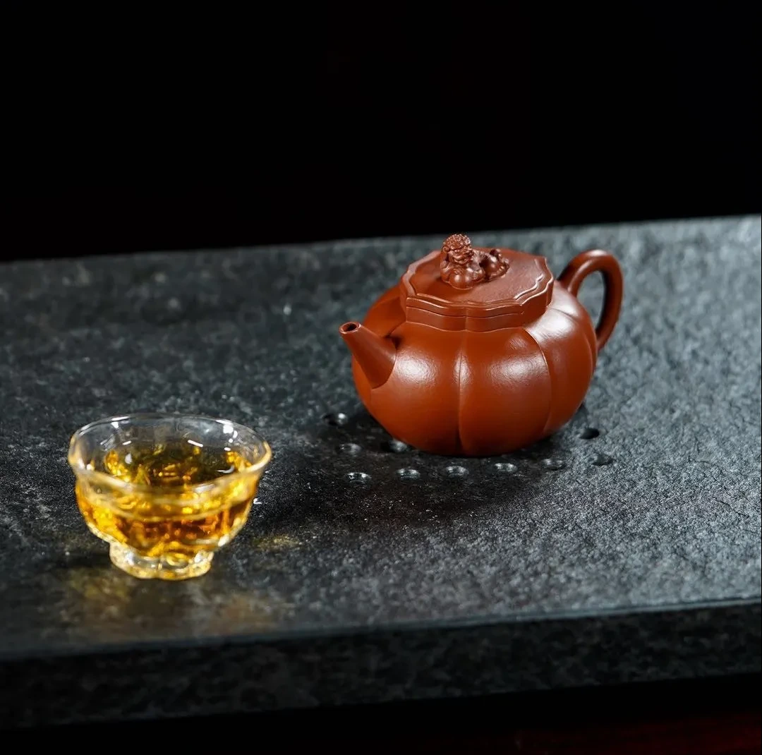 Lobed red clay teapot with a sculpted lid knob beside a glass cup of tea
