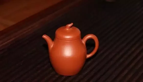Grand rose-orangé argile théière avec un petit bouton incurvé sur un plateau de thé foncé