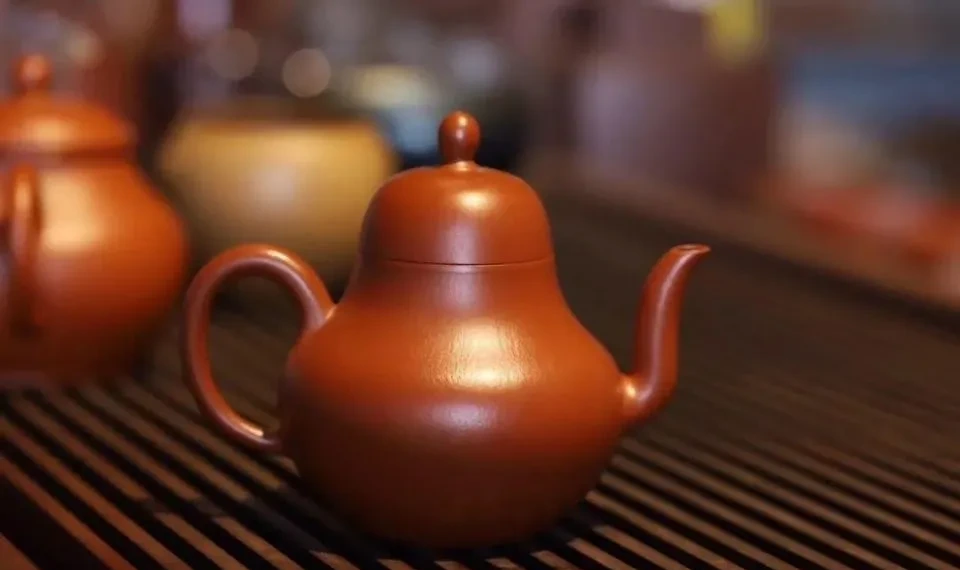 Tall reddish-brown teapot with an upward-curving spout on a slatted tea tray